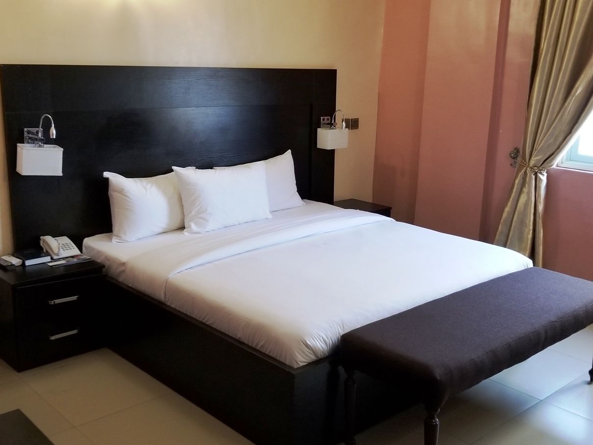 A hotel room with a large bed, a bedside table with a phone, and a bench at the foot of the bed.
