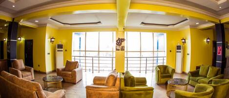 A lobby with yellow walls, multiple seating areas, and large windows.