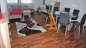 A modern living room with a sofa, coffee table, and dining area with chairs and a table. - Family-friendly apartment on the Hofsteig (Schwarzach)