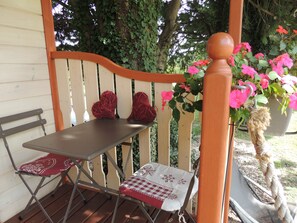 A wooden deck with a table and two chairs, a bench, and a potted plant with pink flowers. -  THE ROULOTTE DU SOLEIL  (Eyragues)