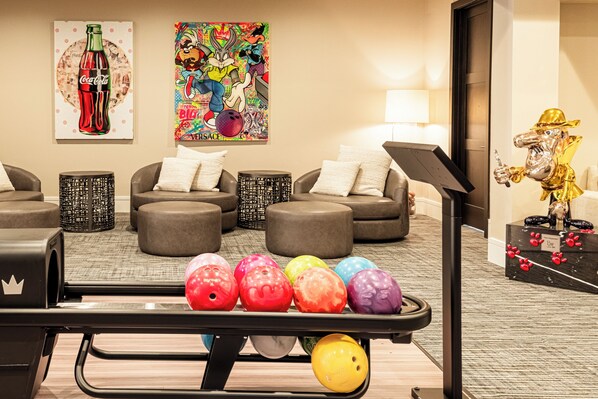 A bowling alley with a pinsetter, colorful bowling balls, and a statue of a character in a hat.