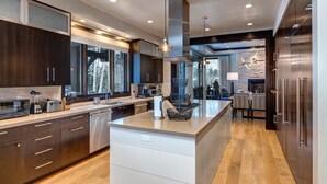 A modern kitchen with dark wood cabinets, a large island, and a stone accent wall. - Ski-in/out Luxury Mansion, Game & Theater Rooms, Private Hot Tubs! Park City Colony Grand (Park City)