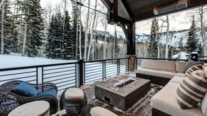 A covered outdoor seating area with a fire feature, wicker furniture, and a view of a snowy forest. - Ski-in/out Luxury Mansion, Game & Theater Rooms, Private Hot Tubs! Park City Colony Grand (Park City)