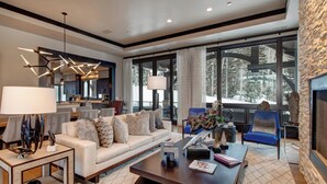 A modern living room with a sofa, coffee table, and chairs. There is a fireplace and large windows with a view of trees. - Ski-in/out Luxury Mansion, Game & Theater Rooms, Private Hot Tubs! Park City Colony Grand (Park City)