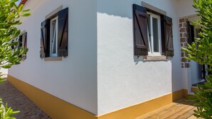 Ein weißes Gebäude mit einem braunen Dach, zwei Fensterläden und einer Holztreppe zum Eingang.