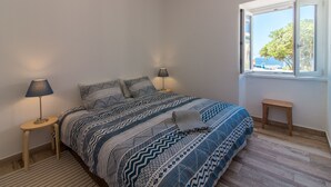 Ein Schlafzimmer mit einem großen Bett, zwei Nachttischen mit Lampen, einem kleinen Hocker und einem Fenster mit Meerblick.