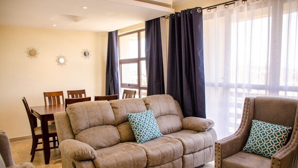 A living room with a beige sofa, two armchairs, a dining table with chairs, and a large window with curtains. - Zawiya property (Nairobi)