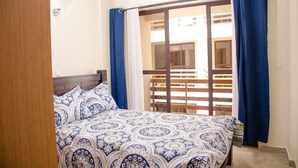 A bedroom with a bed, blue curtains, and a view of a balcony. - Zawiya property (Nairobi)