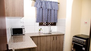 A compact kitchen with a microwave, sink, and stove. - Zawiya property (Nairobi)