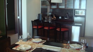 A dining area with a table set for four, a kitchen in the background, and a hanging light fixture.
