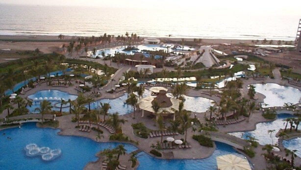 A resort with multiple swimming pools, palm trees, and a beach view.