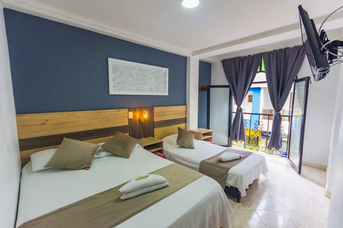 Quarto de hotel com duas camas, uma cabeceira de madeira, televisão fixada na parede e varanda com vista.