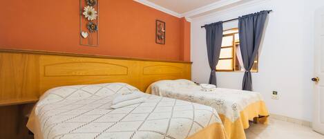 A room with two beds, wooden headboards, a window with curtains, and a door.