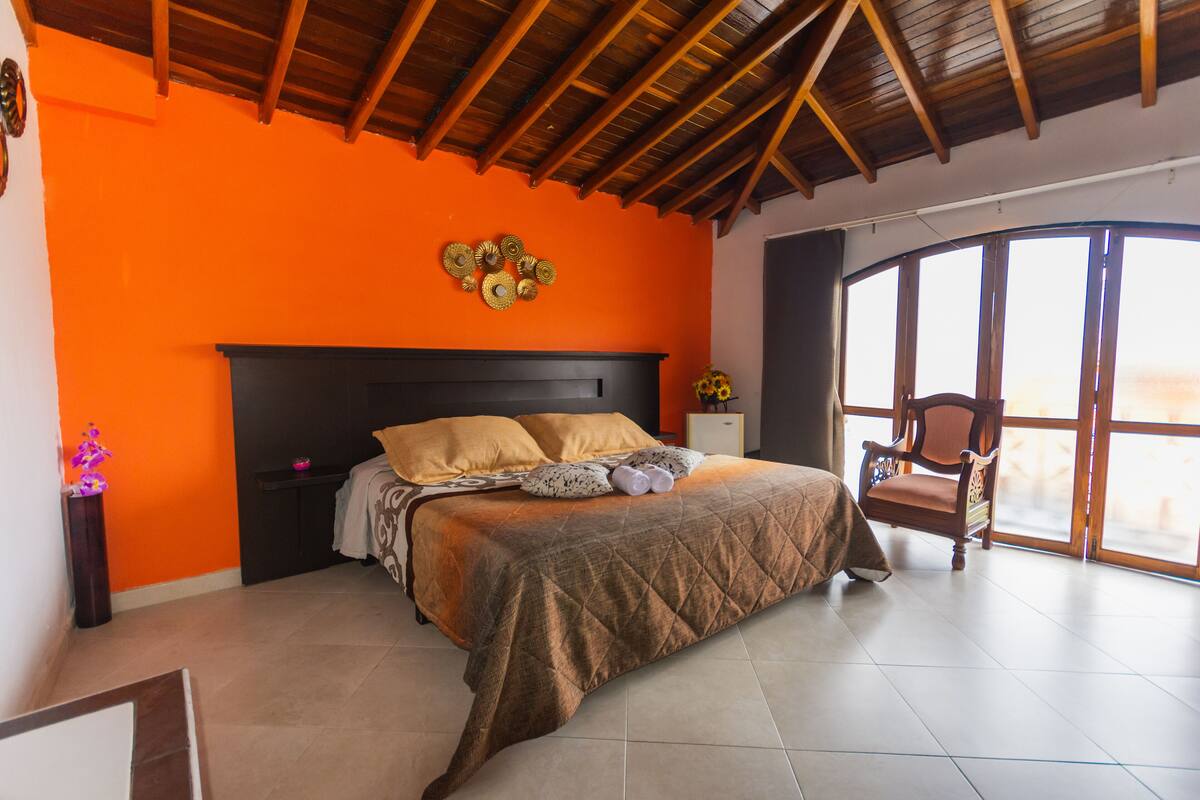Quarto com uma cama grande, teto de madeira e vista através de uma janela ampla.