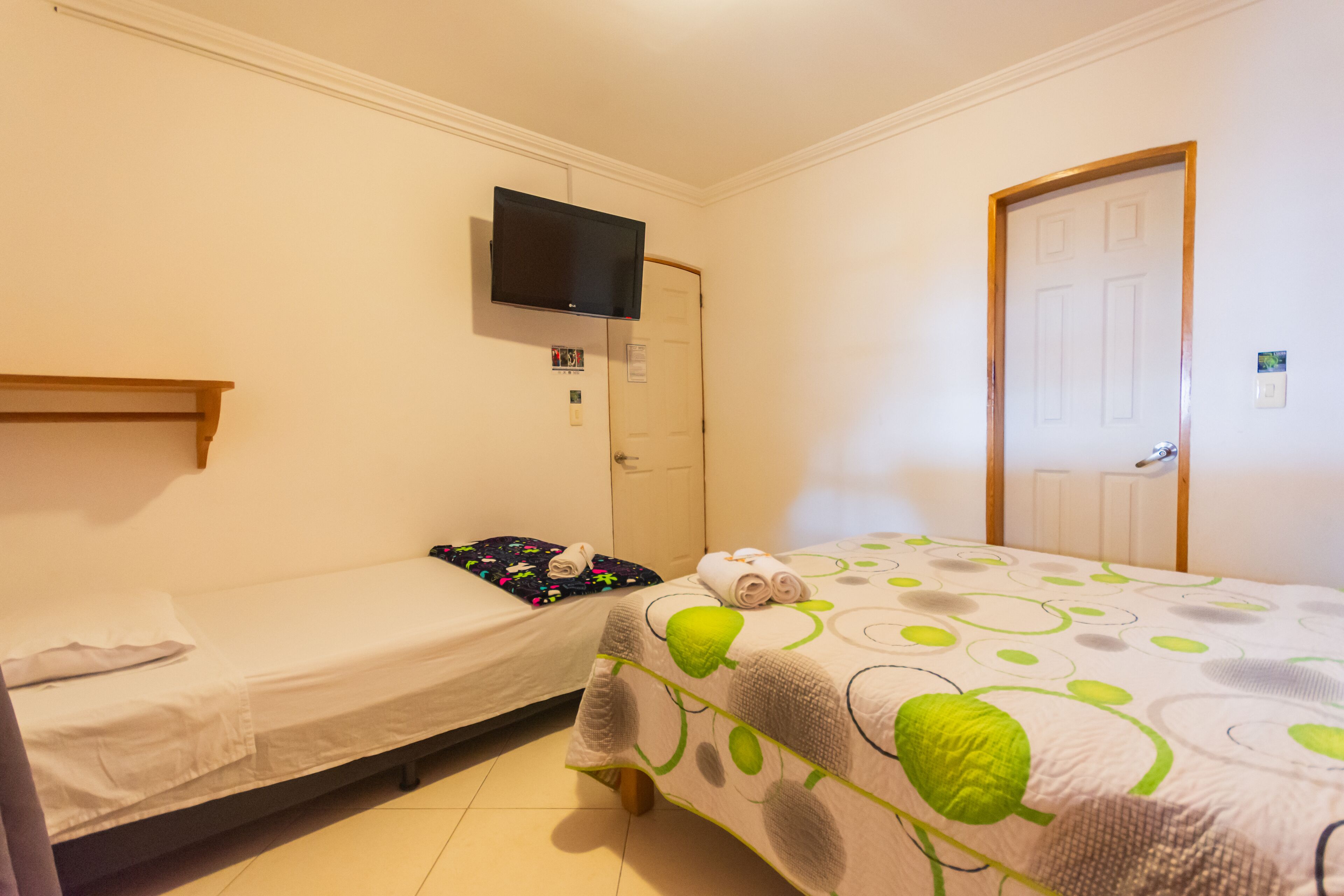 A room with two beds, a television mounted on the wall, and a door.