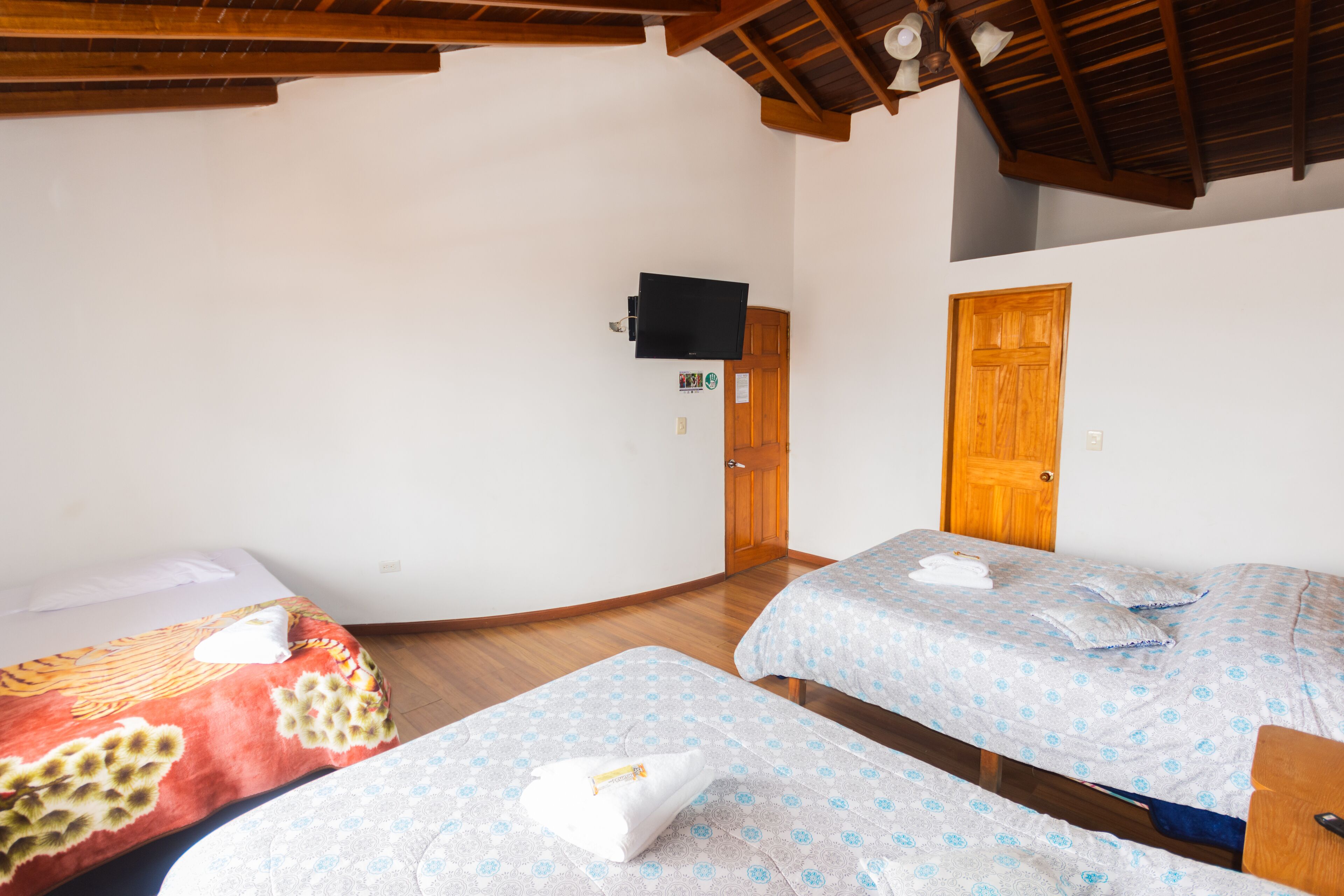 Una habitación con dos camas, vigas de madera en el techo, un televisor en la pared y una puerta de madera.