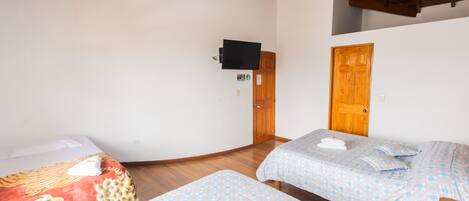 A room with two beds, wooden ceiling beams, a television mounted on the wall, and a wooden door.