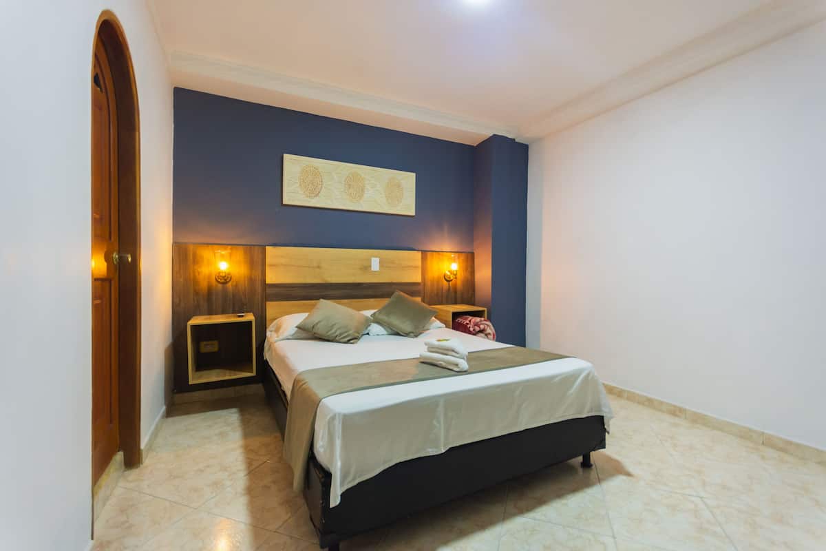 Quarto com cama, duas mesas de cabeceira, uma obra de arte na parede e uma porta.