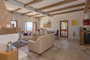 A spacious living area with a high ceiling and exposed wooden beams, a beige sofa, a dining table with chairs, and a view of the outdoors. - Luxury infinity pool villa Pelagos in Hvar town. (Hvar)