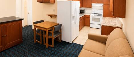 A compact kitchenette with a refrigerator, microwave, stove, and wooden cabinets.