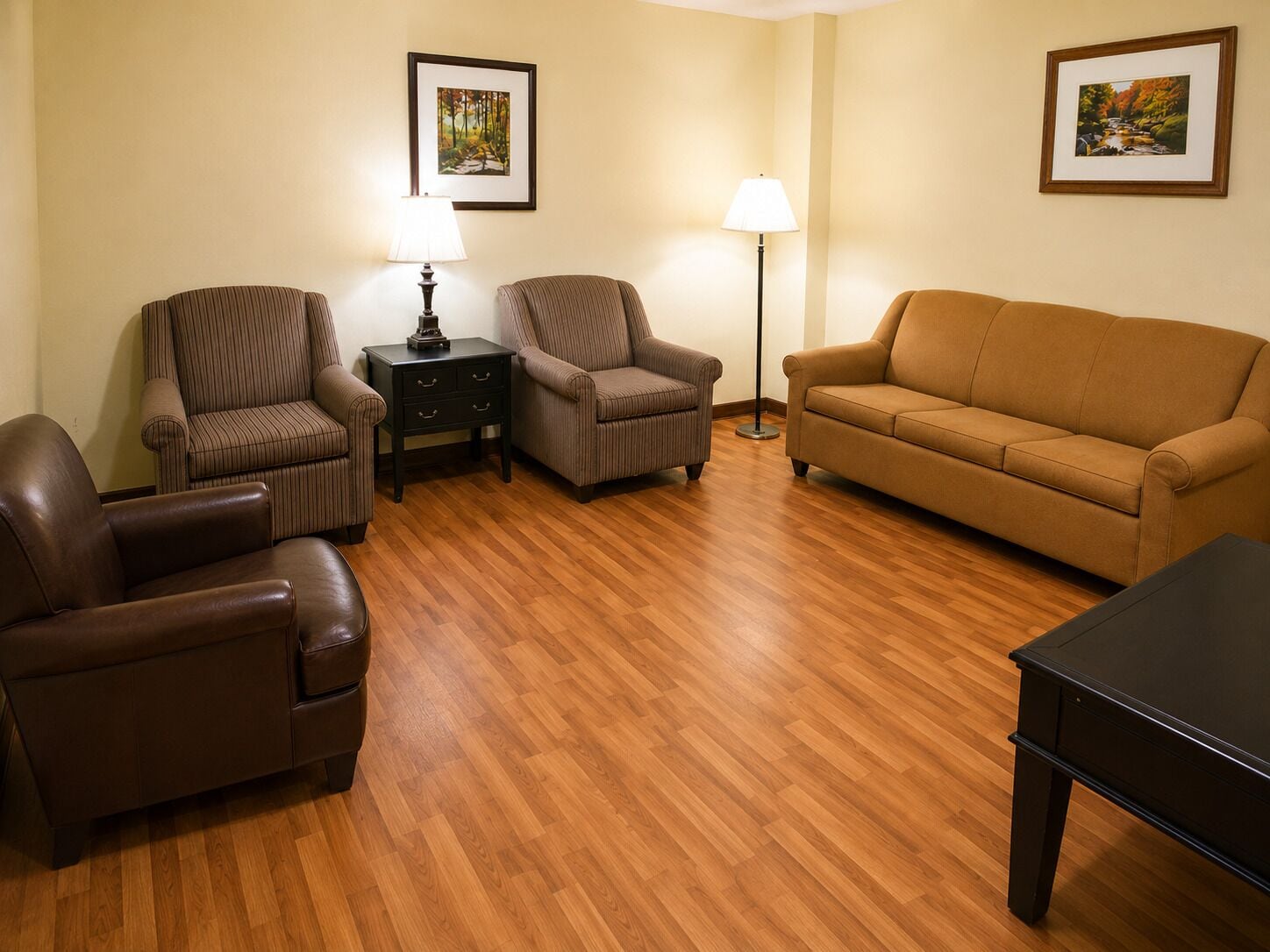 A living room with a brown leather sofa, two armchairs, a small table, and two floor lamps.