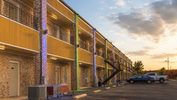 A multi-story motel with a brick facade, balconies, and a parking lot with a few vehicles. - Extended Stay Snyder (Snyder)
