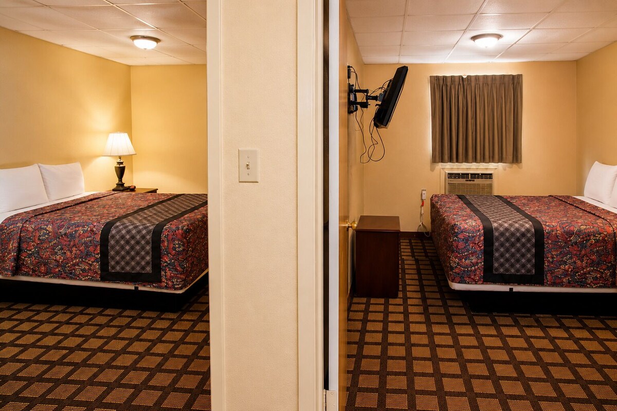 Quarto de hotel com duas camas, uma escrivaninha, abajur, televisão e ar condicionado.