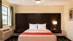 A hotel room with a large bed, two bedside tables, a wall-mounted lamp, and a window with curtains. - Extended Stay Snyder (Snyder)