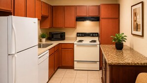 A compact kitchen with wooden cabinets, a white refrigerator, a microwave, an oven, and a sink. - Extended Stay Snyder (Snyder)