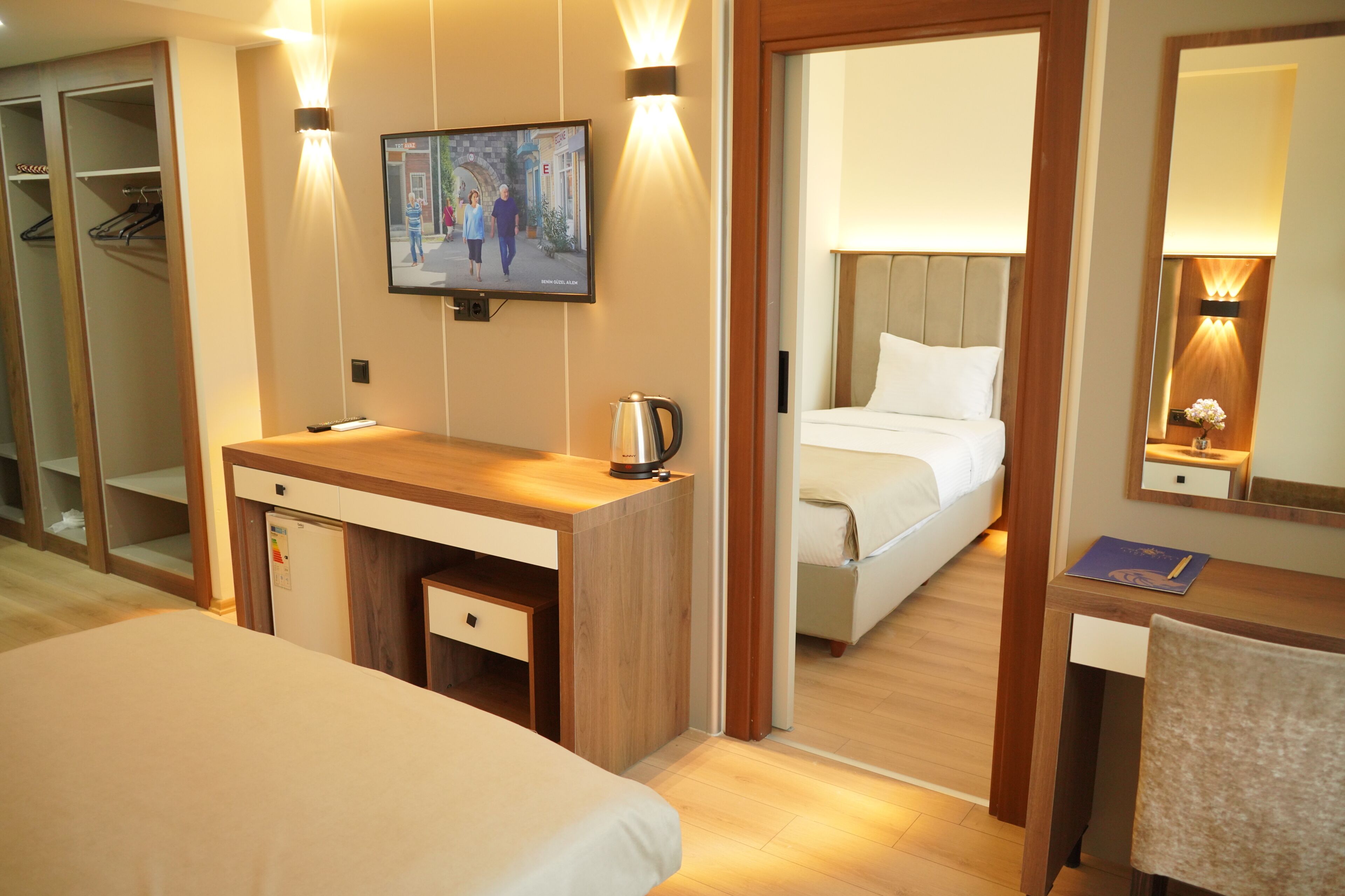 A hotel room with a bed, a desk with a kettle, a TV, and a mirror.