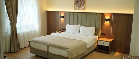 Una habitación de hotel moderna con una cama grande, cabecera de madera, lámparas de noche y una mesita de noche de madera.