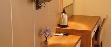 Un escritorio de madera con un espejo, un televisor montado en la pared y un jarrón pequeño con flores.