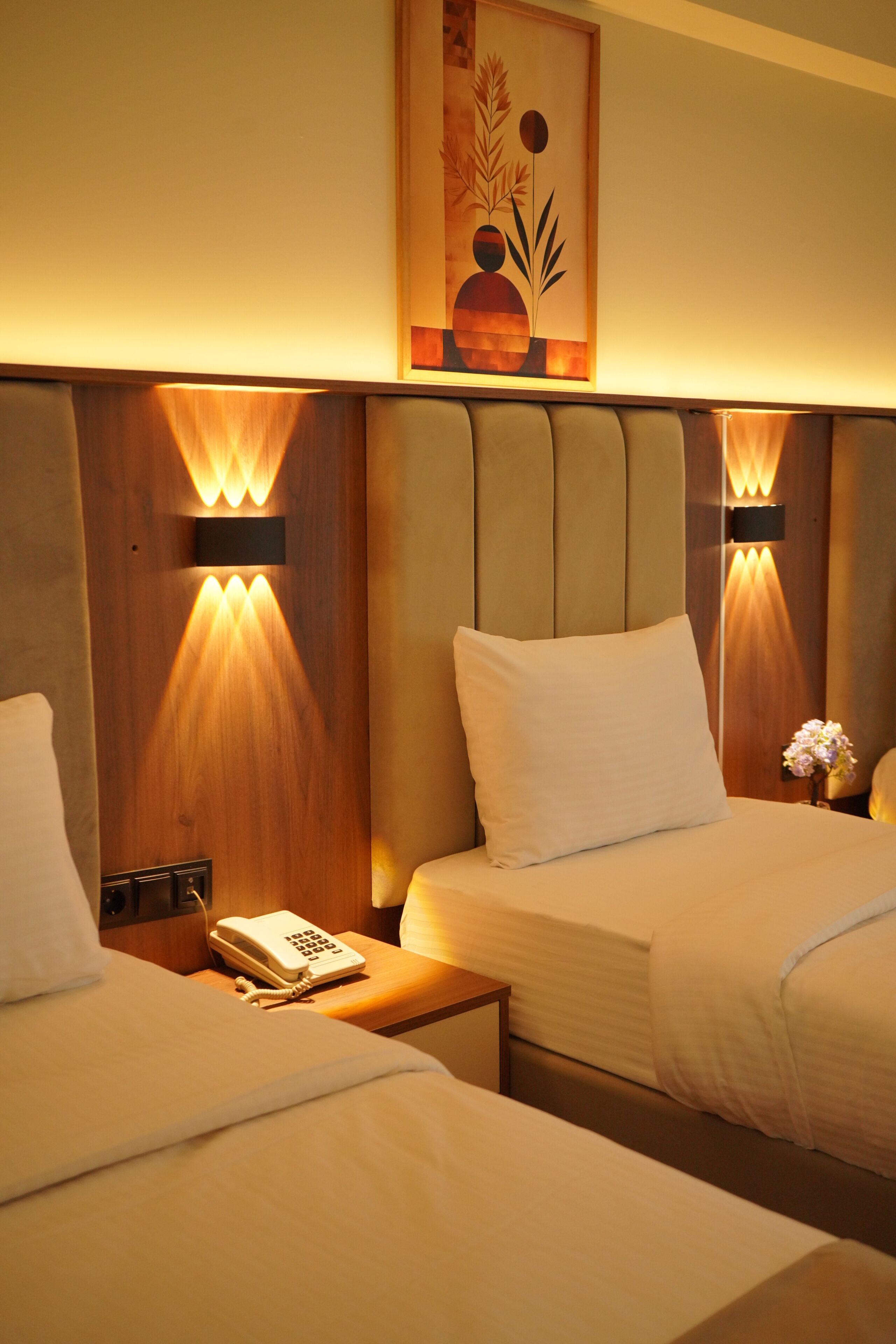 A hotel room with two beds, a bedside telephone, and wall-mounted lighting.