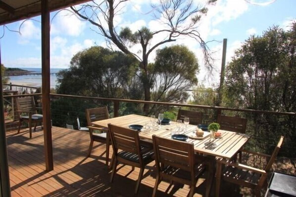 An outdoor dining area with a table and chairs, overlooking a body of water and trees. - Beach front living at Emu Bay (Emu Bay)