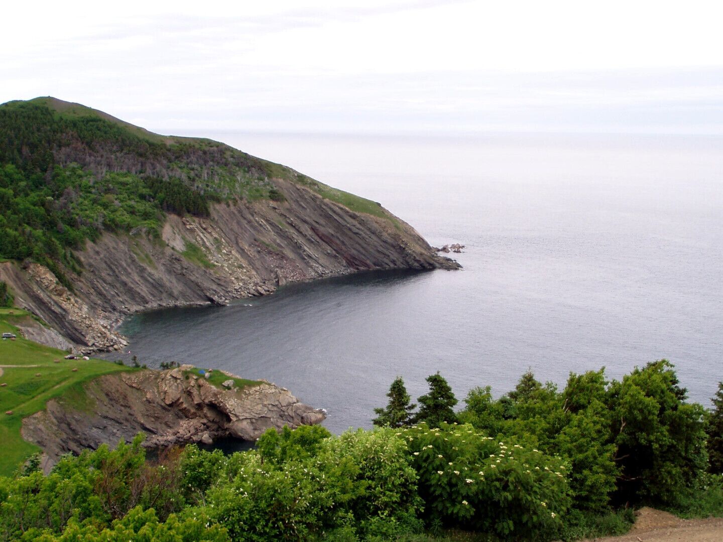 Paesaggio costiero con una scogliera rocciosa e un mare calmo.