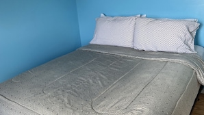 Ein Einzelbett mit einem gemusterten Bettbezug und Kissen, ein Holz-Kopfteil und eine blaue Wand.
