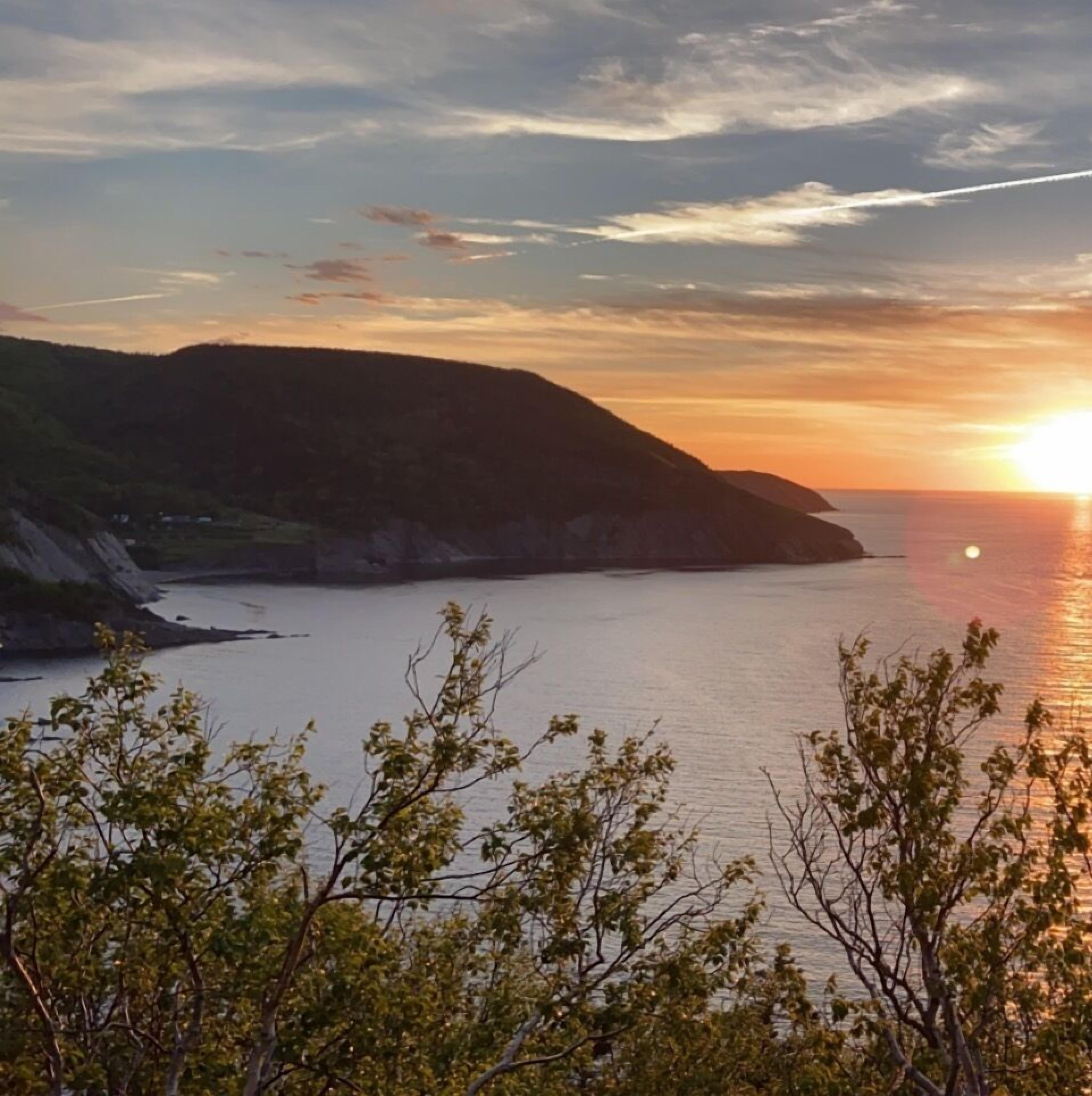A coastal landscape with a sunset, hills, and a body of water.