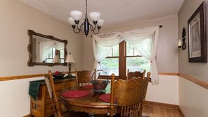 Une salle à manger avec une table en bois, des chaises, un lustre, un miroir et une fenêtre ornée de rideaux légers.
