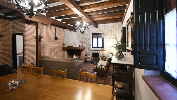 Ein rustikaler Innenraum mit freiliegenden Holzbalken, einer Backsteinwand, einem Kamin und einer Essecke mit Holzmöbeln.