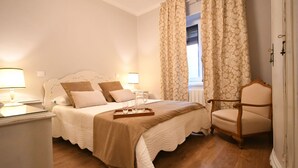 Ein ordentlich eingerichtetes Schlafzimmer mit einem Bett, Nachttischlampen, einem Sessel und einem Fenster mit Vorhängen.