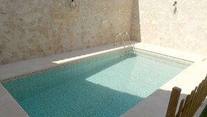 Ein rechteckiger Swimmingpool mit einer gefliesten Kante, umgeben von einer weißen Terrasse und einem Holzzaun.