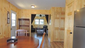 A wooden interior with a dining table, chairs, a refrigerator, and a seating area with sofas and a coffee table.