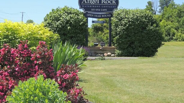 A sign for Angel Rock Waterfront Cottages with a 'Vacancy' label, surrounded by lush greenery and a well-maintained lawn.