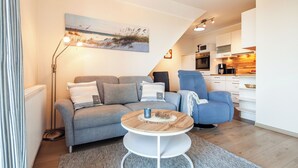 A modern living room with a grey sofa, a blue armchair, and a round coffee table. A painting of a beach scene hangs on the wall.
