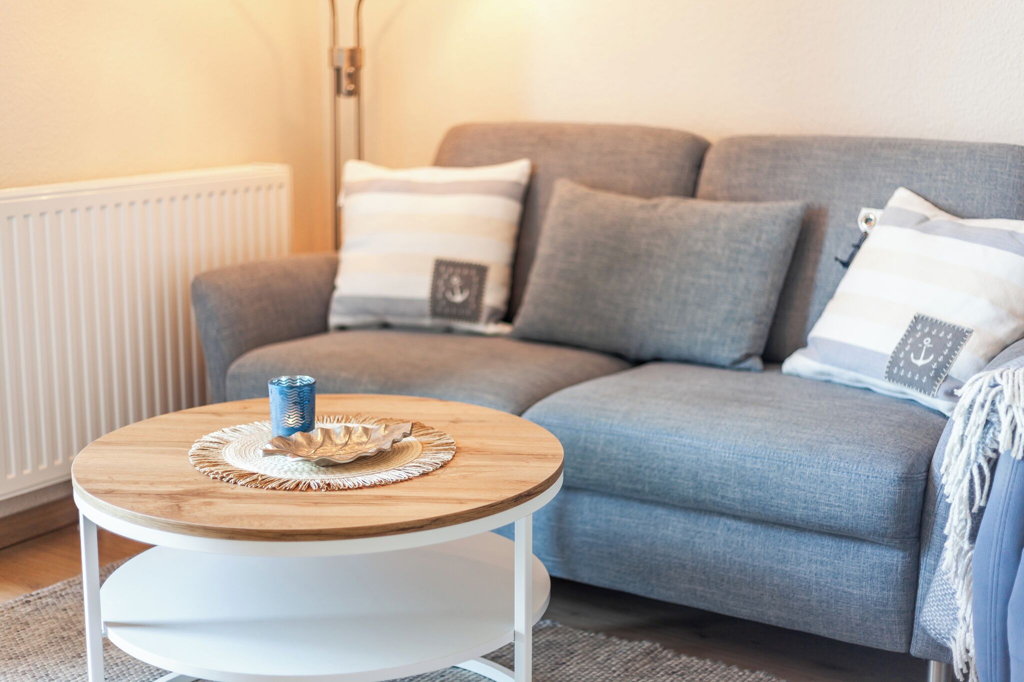 Ein modernes Wohnzimmer mit grauem Sofa, einem runden Couchtisch aus Holz und einem weißen Heizkörper.