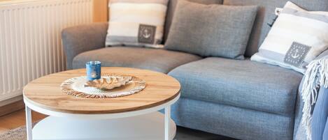 Ein modernes Wohnzimmer mit grauem Sofa, einem runden Couchtisch aus Holz und einem weißen Heizkörper.