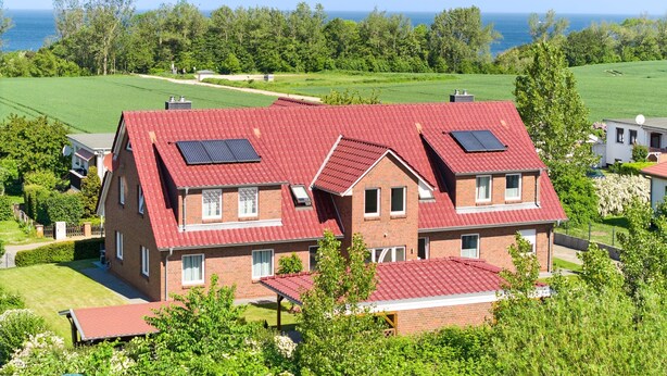 A two-story house with a red roof, solar panels, and a view of the ocean.