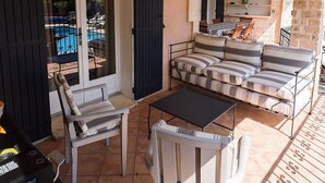 An outdoor patio with a sofa set, a table, and chairs. There is a pool visible through the glass doors.