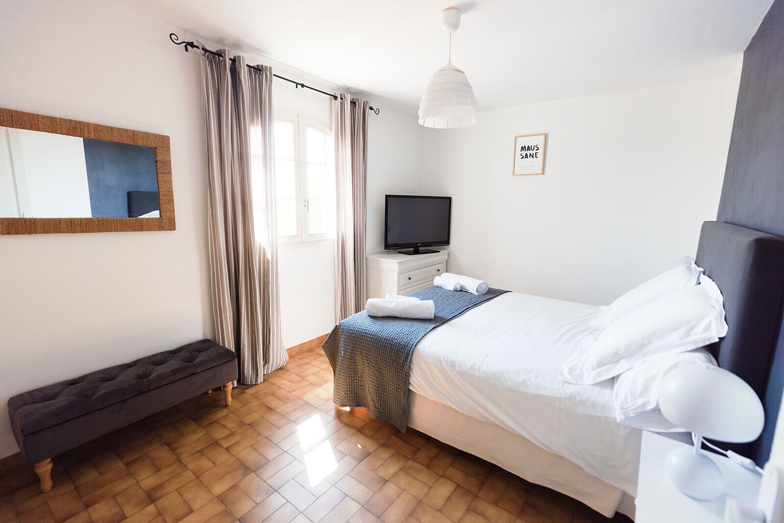 Een moderne slaapkamer met een bed, een televisie, een bankje en een spiegel.