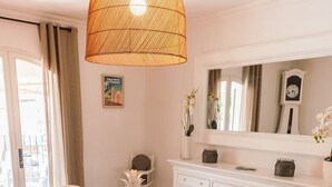 A dining area with a round table, white chairs, woven placemats, a white vase, and a hanging light fixture.